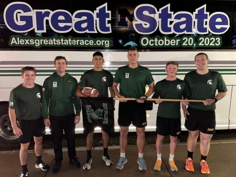 Six MSU Army ROTC Cadets standing in front of the AGSR transportation bus holding the game ball and ready to begin the race