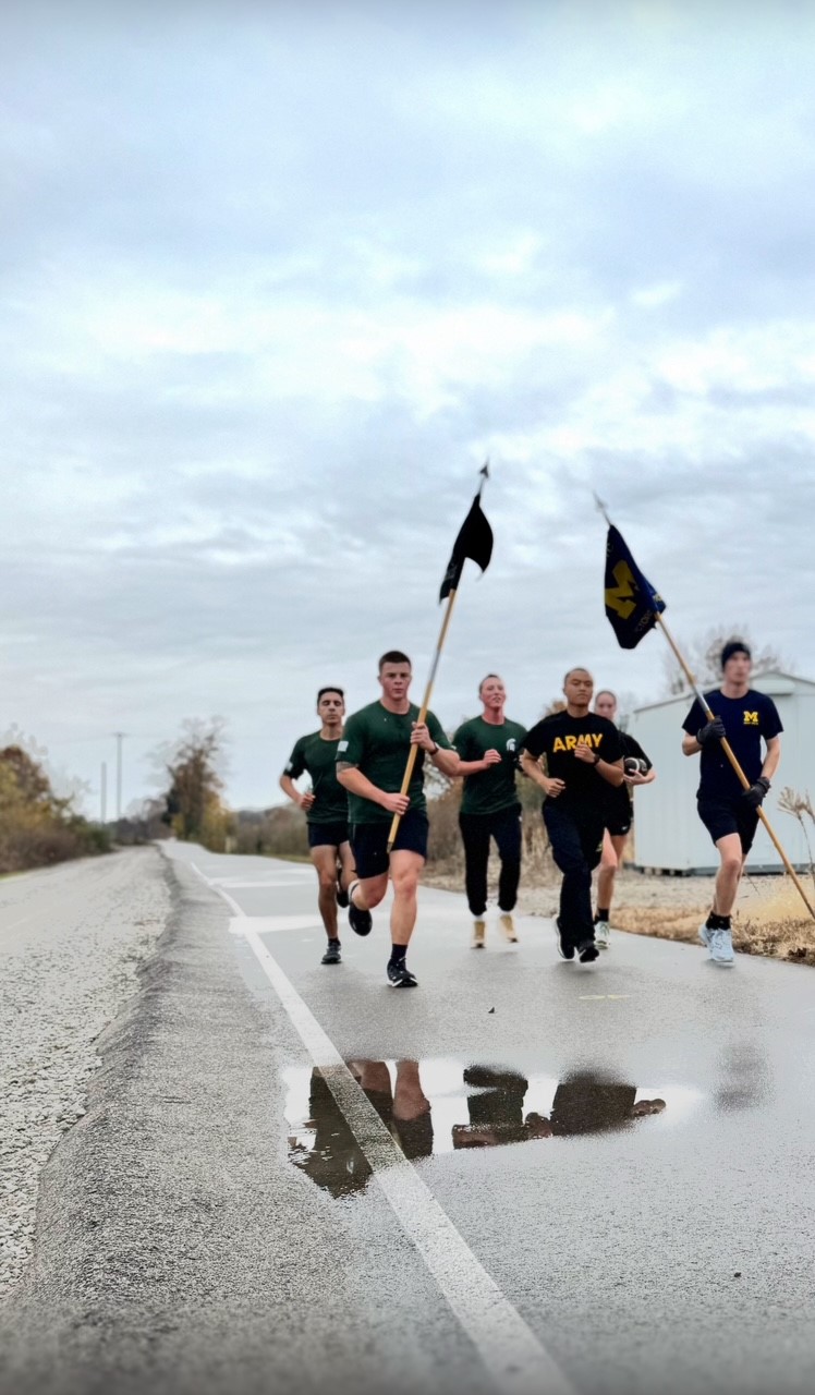 UM and MSU runners carrying flags on a wet backroad in MI